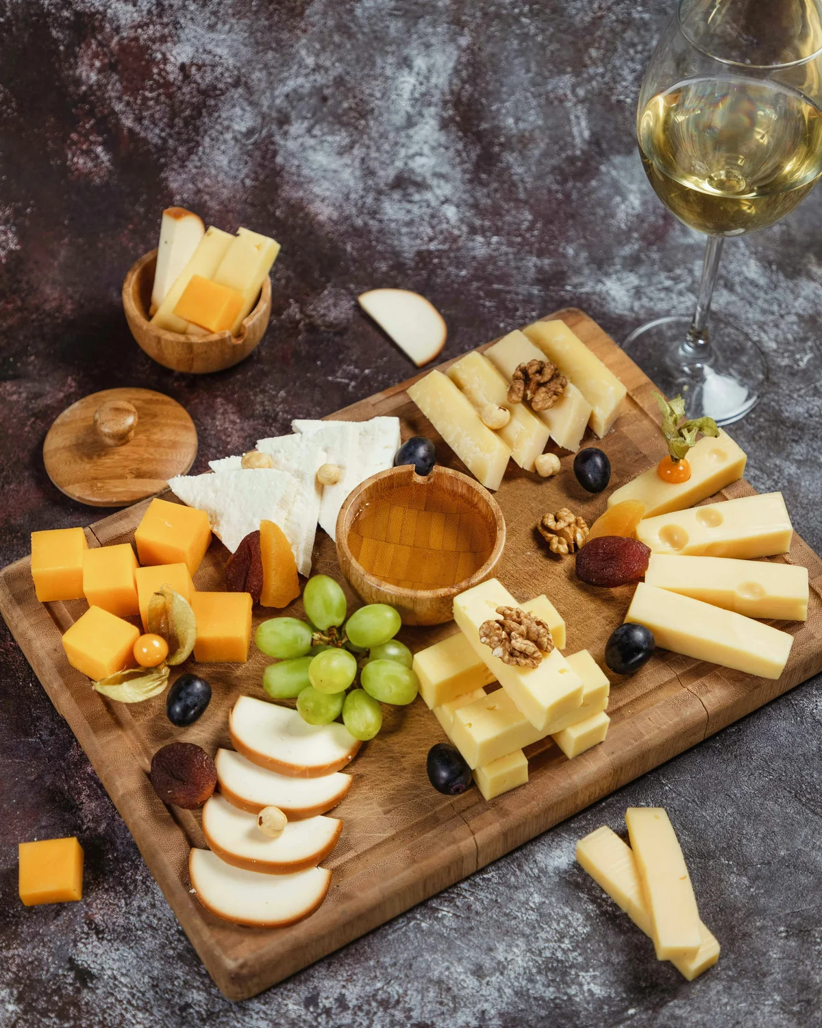 A cheese board with walnuts, grapes, honey and a glass of wine